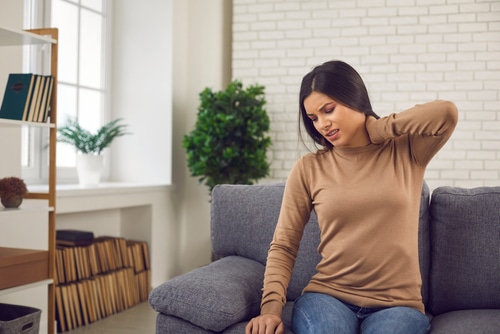 woman sitting on couch holding neck due to chronic pain